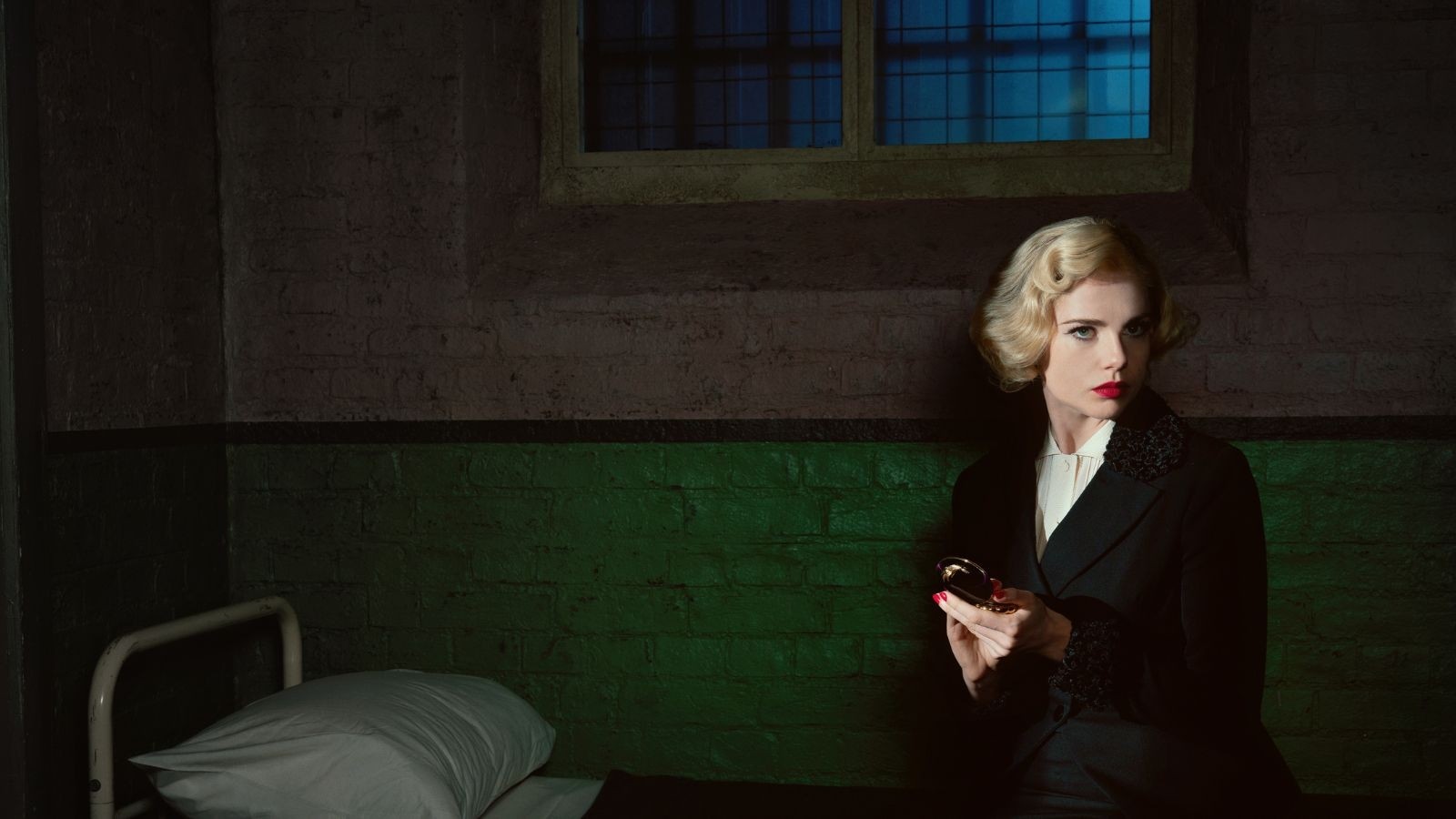 Lucy Boynton as Ruth Ellis sat on a prison bed with red lipstick on